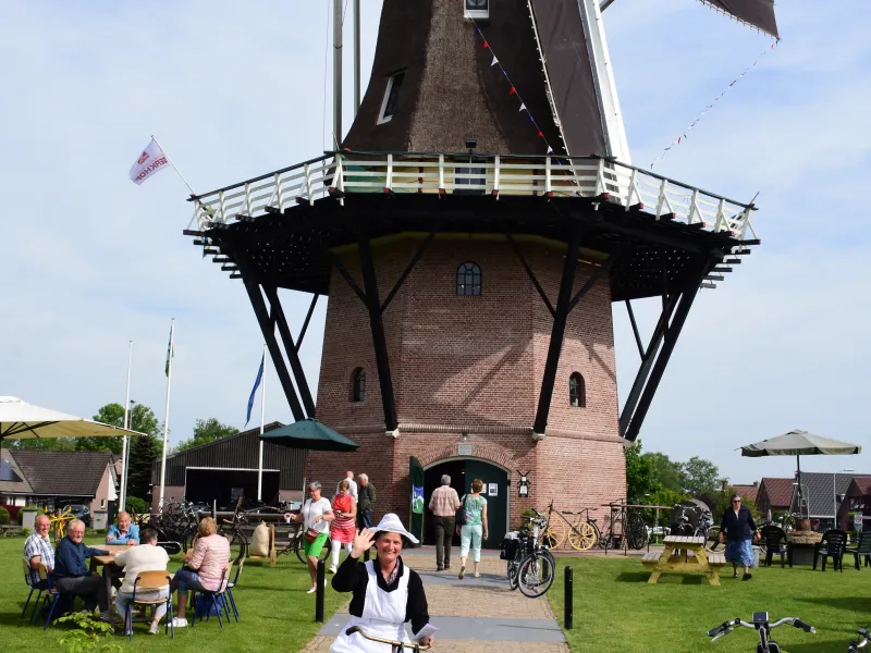 Molen met daarvoor een dame in oude klederdracht op fiets.