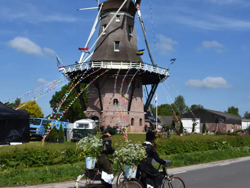 Twee fietsers in klederdracht fietsen langs de Puurveense Molen