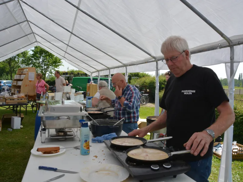 Meerdere vrijwilligers staan in de tent pannenkoeken te bakken