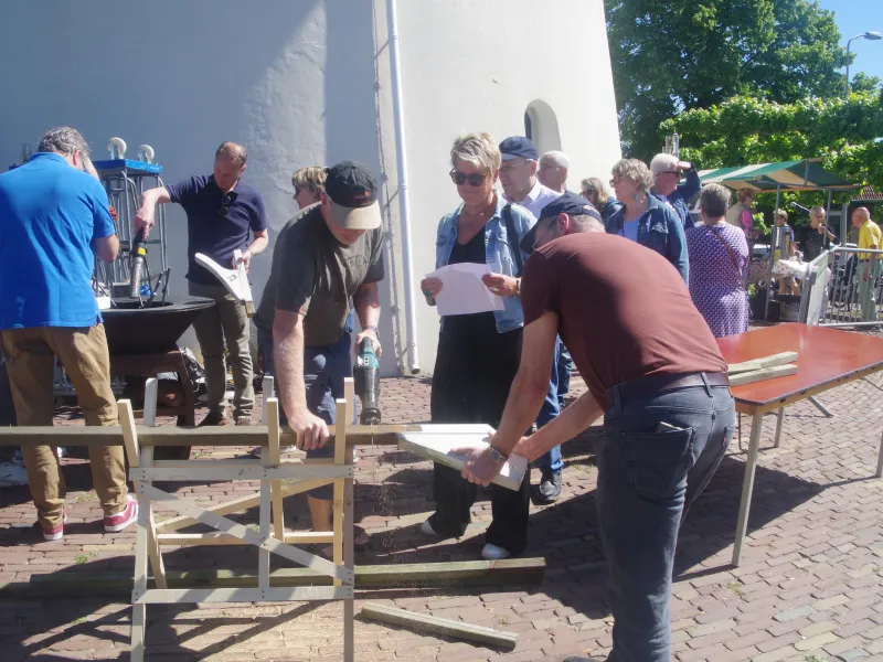 Buiten bij de molen. Een aantal mannen staan de heklatten van de molen te zagen
