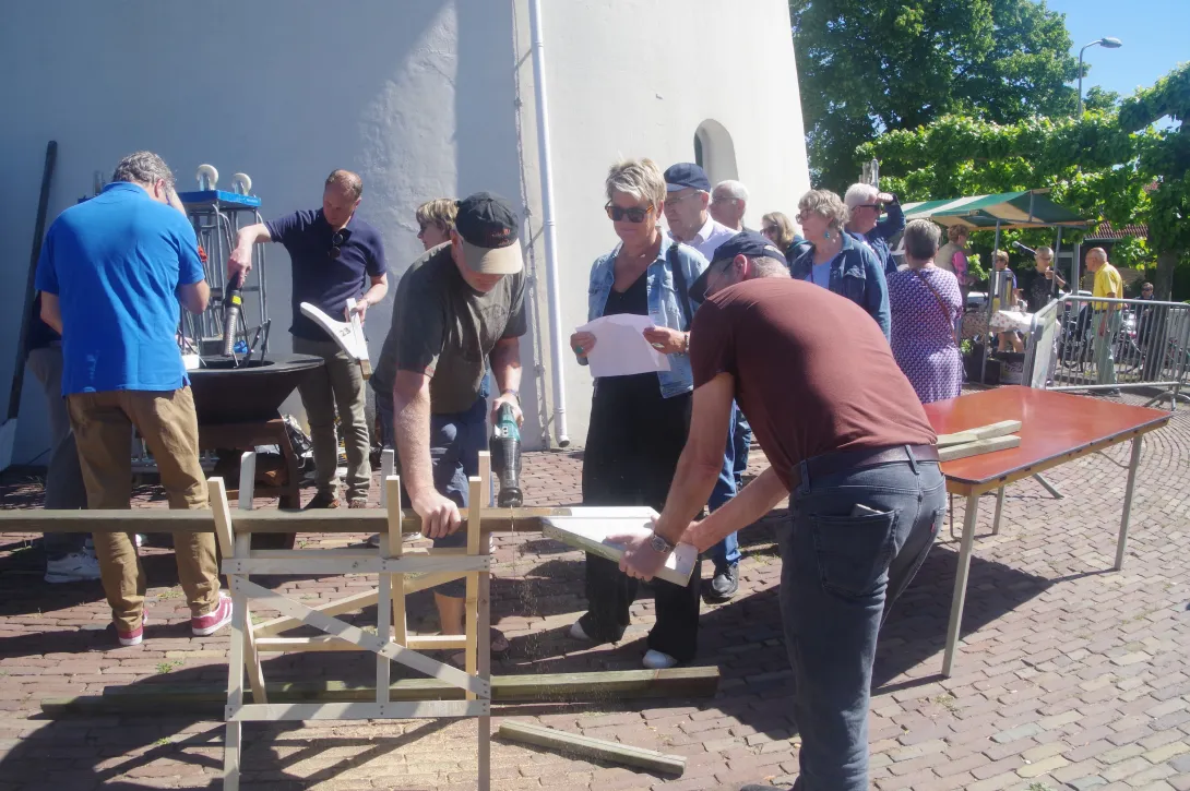 Buiten bij de molen. Een aantal mannen staan de heklatten van de molen te zagen